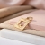 Pozłacana srebrna zawieszka z ażurową ramką i cyrkonią – leżąca na jasnej tkaninie i różowej płytce
