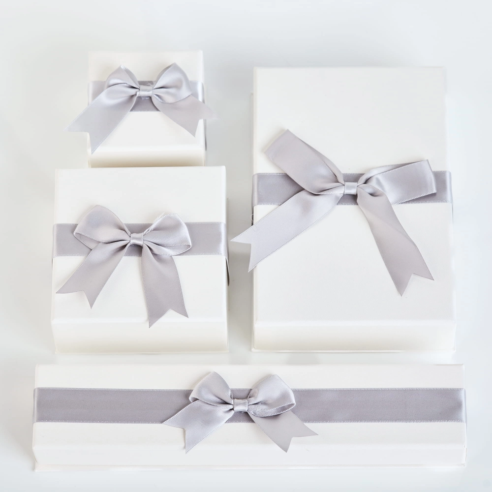Białe pudełka jubilerskie NOVADI z szarymi kokardami ustawione pionowo