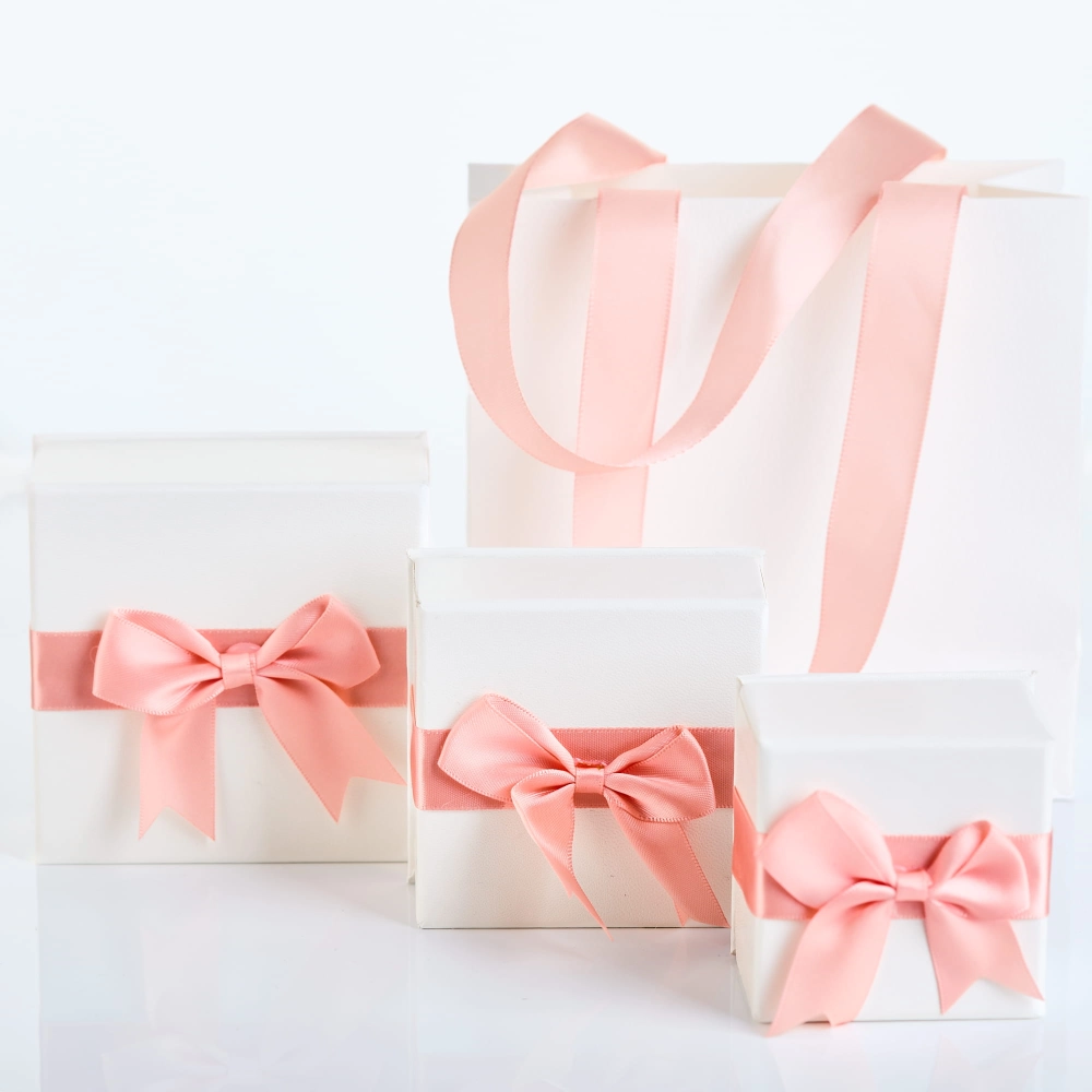Białe torby i pudełka prezentowe NOVADI z różowymi kokardami